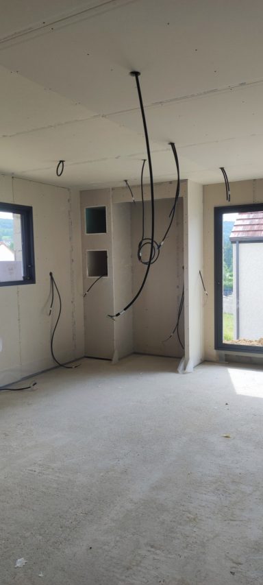 Pièce intérieure avec murs en béton, câblage électrique exposé et fenêtres.